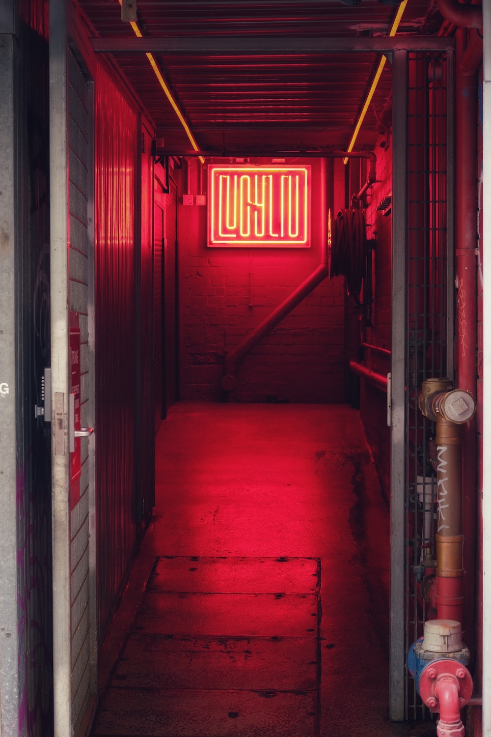 An industrial looking restaurant doorway with red neon lights.