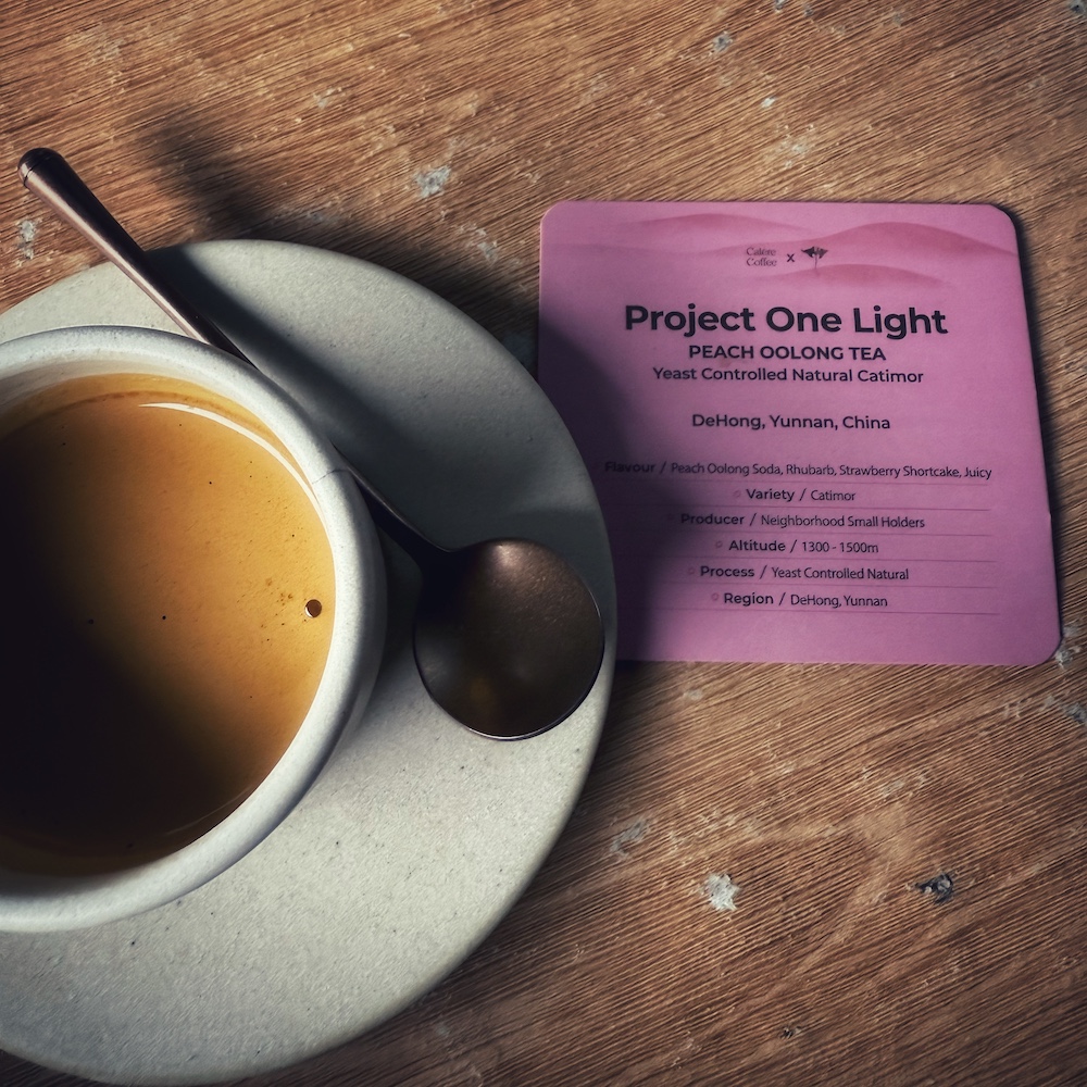 A double espresso in a cup. Next to it is a card with the tasting notes. The coffee is Project One Light - Peach Oolong Tea, a yeast controlled Natural Catimor from DeHong, Yunnan, China.