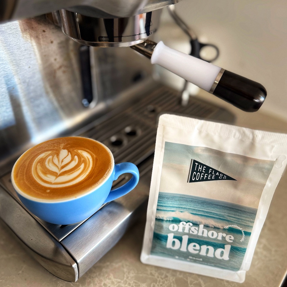 A flat white coffee with latte art on the coffee machine. The bag next to it says The Flag Coffee Co - Offshore Blend.