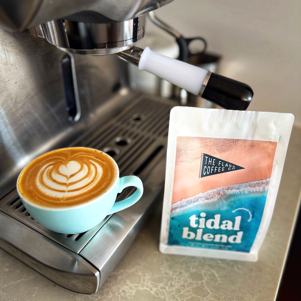 A flat white coffee with latte art on the coffee machine. The bag next to it says The Flag Coffee Co - Tidal Blend.