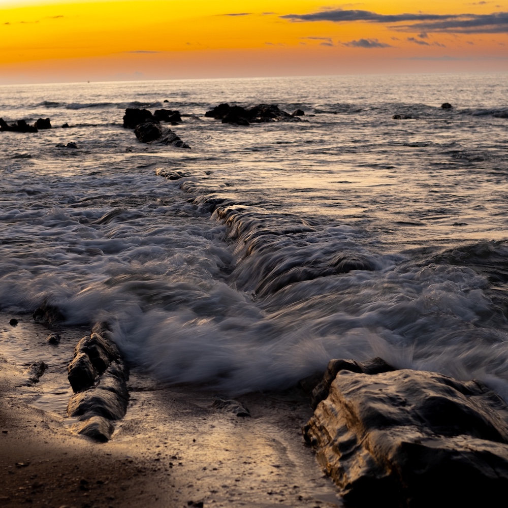 Waves flowing over rocks on the beach at sunset.